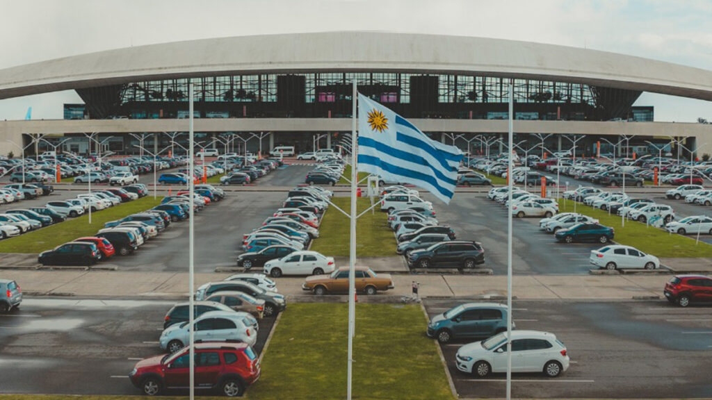 Aeropuerto de Carrasco avanza en accesibilidad con certificación internacional de Nivel 2 Aeropuerto Internacional de Carrasco en Montevideo, Uruguay, con su estacionamiento y la bandera nacional en primer plano.