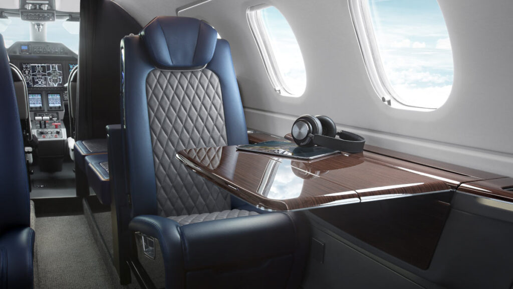 Interior de la cabina de pasajeros del jet ejecutivo Embraer Phenom 300EV con asientos de cuero, mesa desplegable y vista a la cabina de mando.