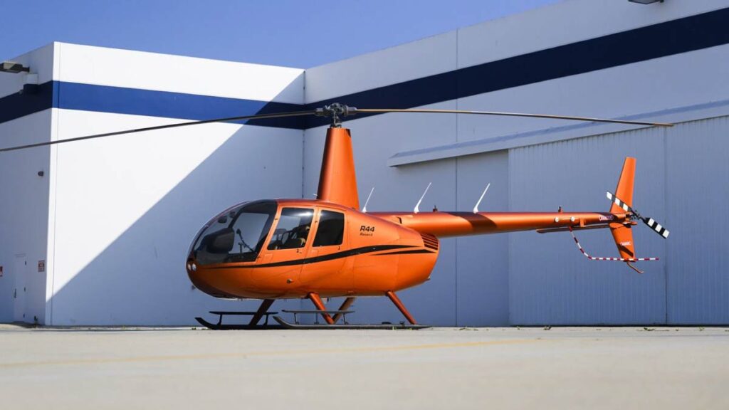 Robinson Helicopter entrega la unidad 5.000 del modelo R44 Raven II Helicóptero civil ligero Robinson R44 Raven II color naranja estacionado en la plataforma de hormigón frente a un hangar
