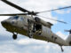 Helicóptero militar utilitario UH-60 Black Hawk en vuelo con la compuerta lateral abierta y tripulación a bordo.
