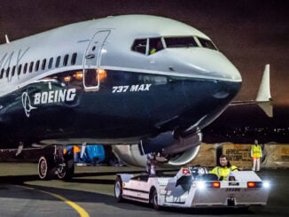 Avión Boeing 737 MAX con colores de fábrica siendo remolcado por un tractor de empuje operado por personal de tierra durante la noche