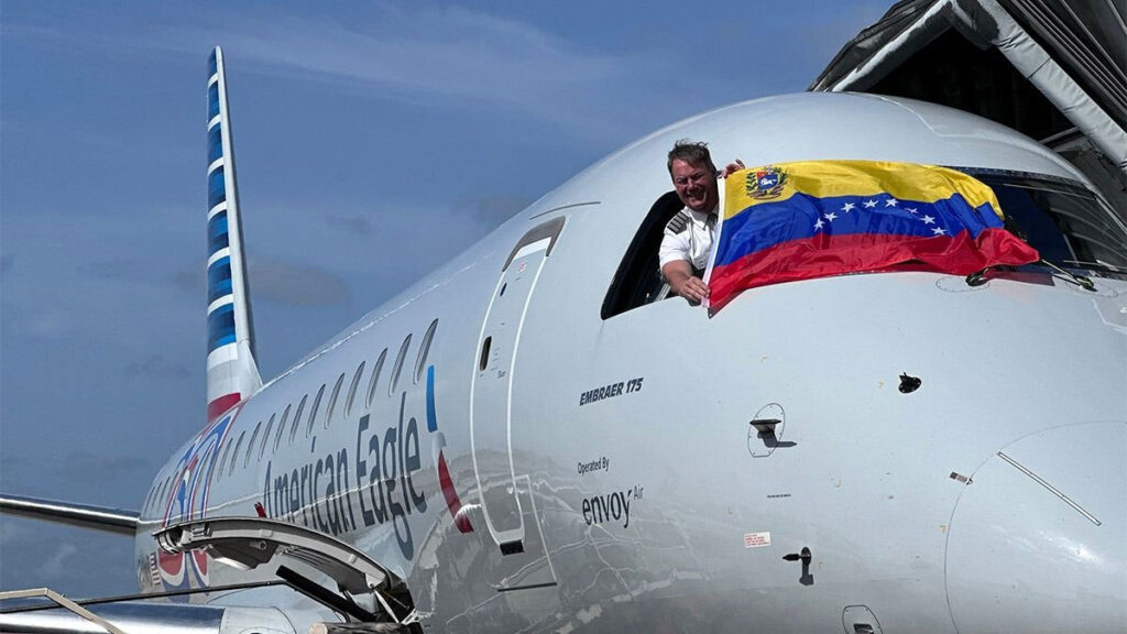 American Airlines expande su red en Venezuela con una nueva ruta a Barcelona desde Miami Piloto de American Eagle asomado desde la cabina de un Embraer 175 exhibiendo la bandera de Venezuela, celebrando la expansión de rutas hacia Barcelona desde Miami.