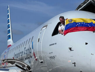 Piloto de American Eagle asomado desde la cabina de un Embraer 175 exhibiendo la bandera de Venezuela, celebrando la expansión de rutas hacia Barcelona desde Miami.