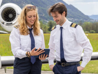 Dos pilotos de aviación ejecutiva revisando planes de vuelo y datos operativos en una tablet junto a una aeronave, ilustrando la conectividad en tiempo real.