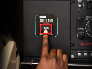 Primer plano de una mano presionando el botón rojo de emergencia del sistema Garmin Autoland en el panel de instrumentos de un avión.