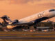 Avión regional Bombardier CRJ-200 con el esquema de pintura de JOY Airline despegando de la pista de un aeropuerto al atardecer.