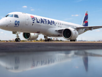 El primer avión comercial Embraer E195-E2 con el diseño y los colores de LATAM Airlines estacionado en la plataforma, reflejado sobre una superficie húmeda en primer plano.