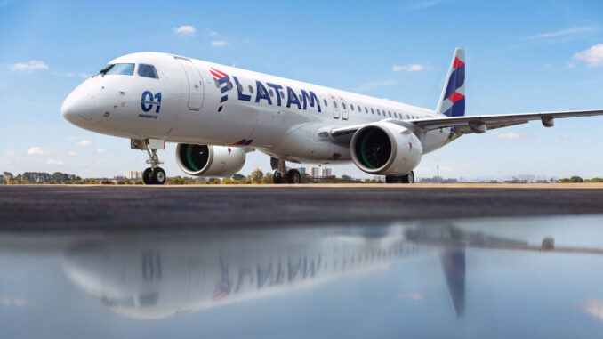 El primer avión comercial Embraer E195-E2 con el diseño y los colores de LATAM Airlines estacionado en la plataforma, reflejado sobre una superficie húmeda en primer plano.
